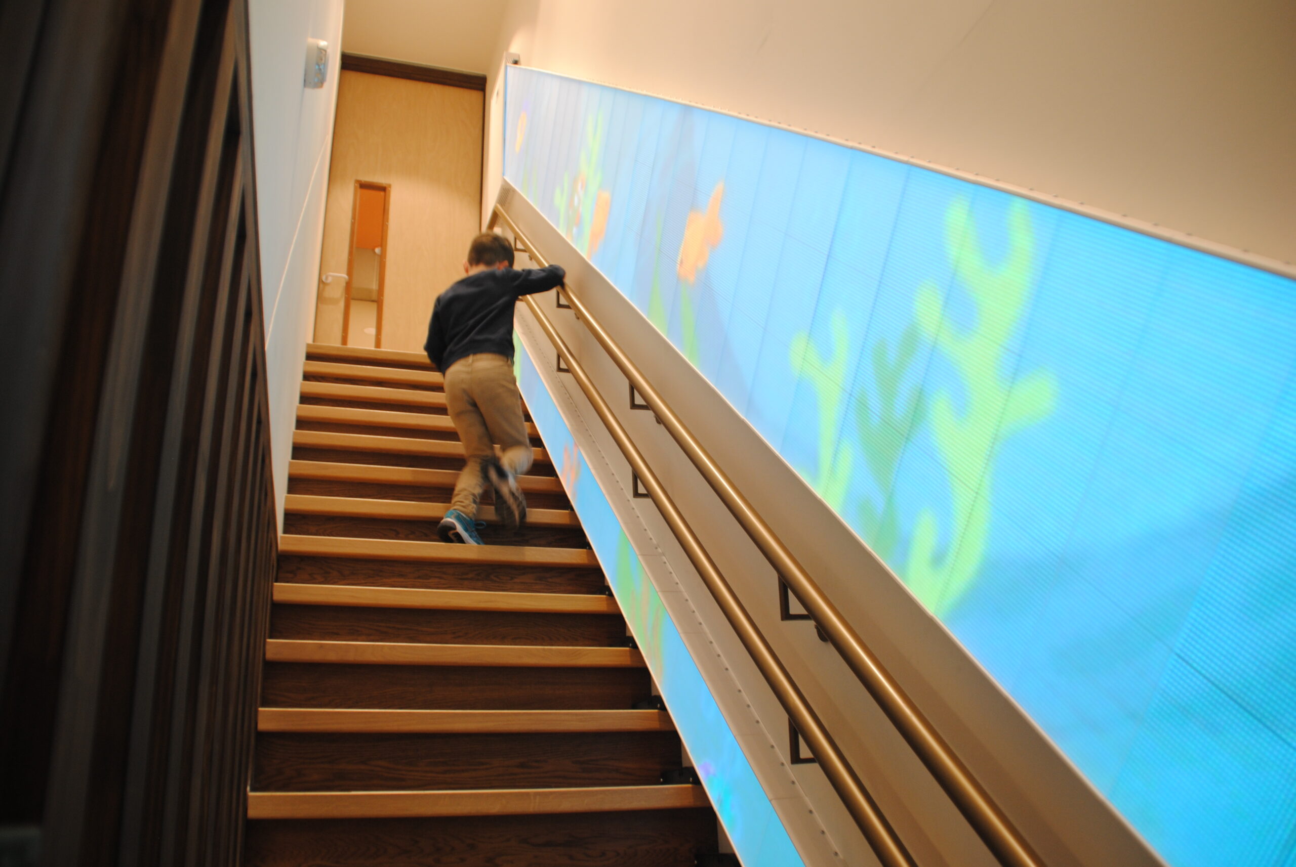 Kind loopt de belevenistrap op met een aquariumanimatie op LED-panelen ter ondersteuning van revalidatie