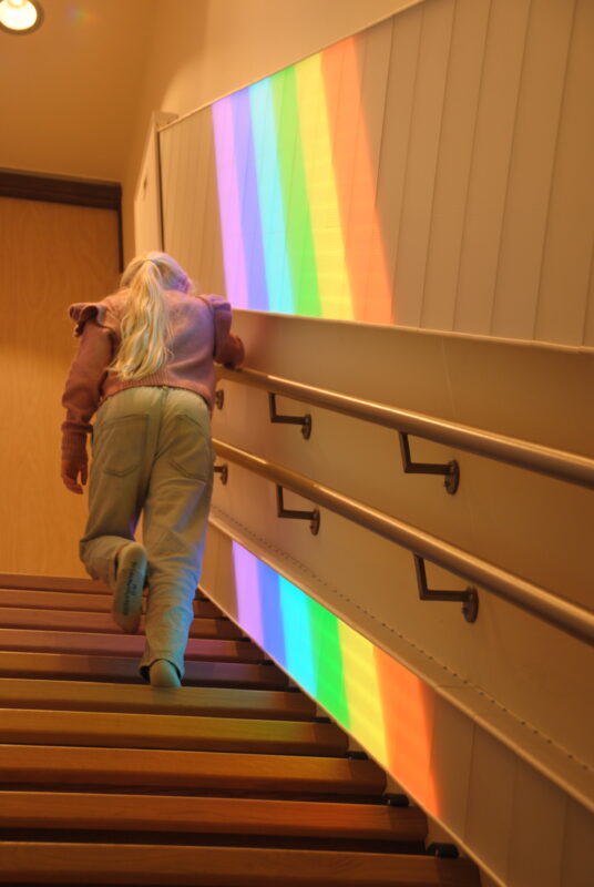 Kind loopt de belevenistrap op terwijl de interactieve regenbooganimatie per trede van kleur verandert